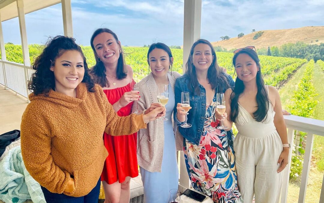 group of woman holding up glasses with vineyards behind